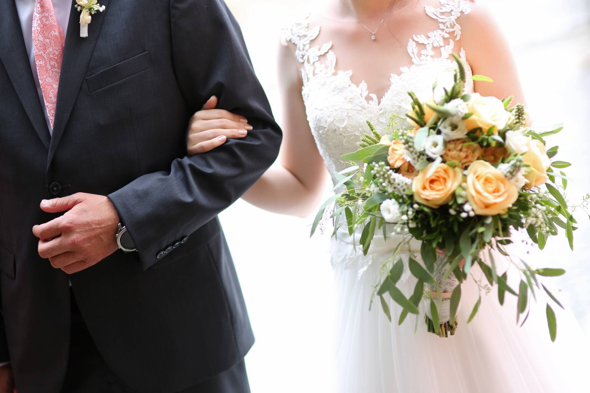 Braut und Vater betreten die Kirche. Vater in Anzug mit rosa Kravatte. Braut in weißem Kleid mit Rosenstrauß.